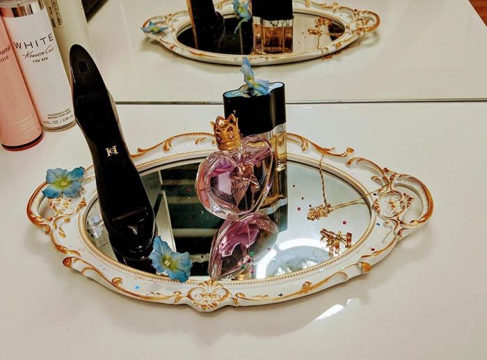 Perfume and other small items arranged on a white and gold mirror being used as a tray