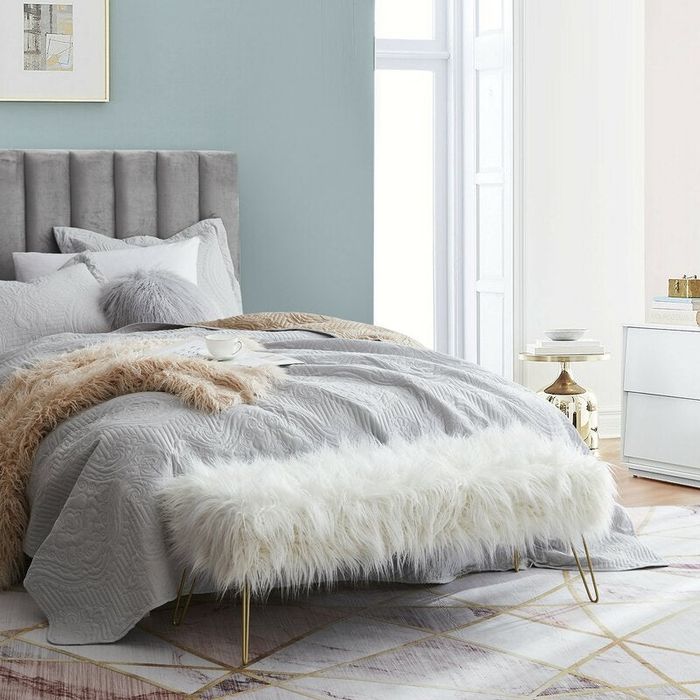 a lifestyle photo of a fuzzy white bench at the foot of the bed