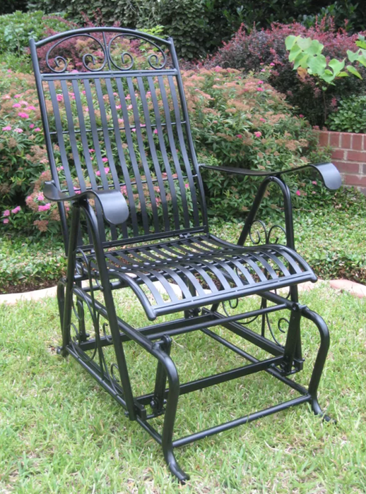 A curved wrought iron gliding chair placed on grass outside