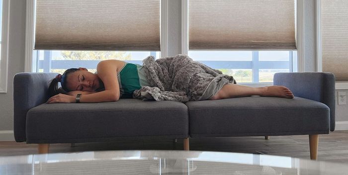 The same reviewer lounging on the gray sofa, now folded out into a bed, showing its dual function.