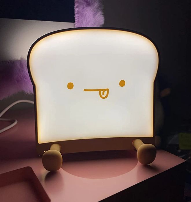 Reviewer's glow-in-the-dark toast night light with its tongue sticking out, glowing in a dim bedroom