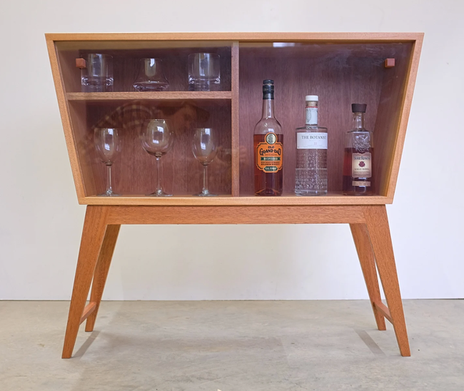 Light wood retro-style bar cabinet with an angular design, neatly stocked with bottles and glassware