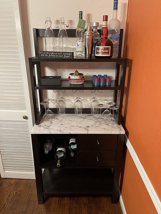 Reviewer image of a wooden and faux marble bar cabinet with bottles arranged in cubbies and atop shelves