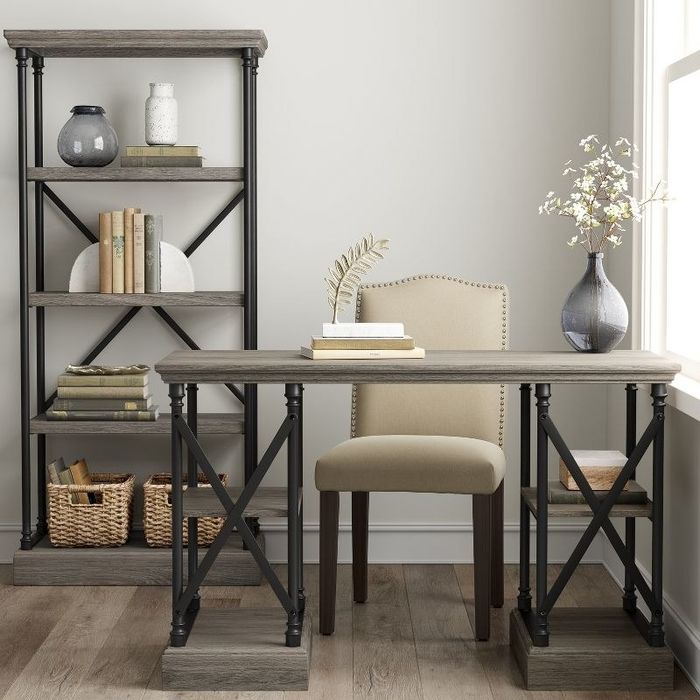 A gray wood writing desk placed next to a tufted chair and a stylish bookcase, creating a chic study nook.