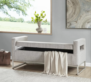 the gray storage bench, slightly ajar, with a blanket peeking out from inside