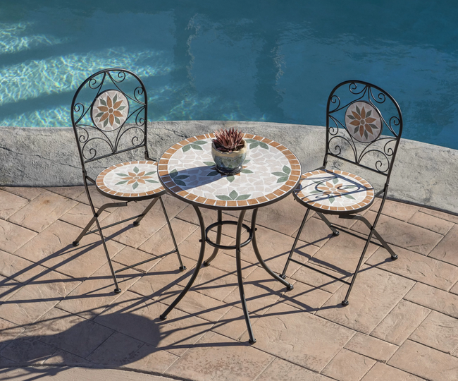 Black, orange, and green mosaic bistro chairs surrounding a round table next to a pool