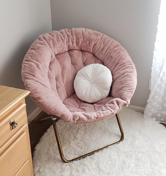 A photo of a pink saucer chair with a white pillow, giving off cozy vibes.