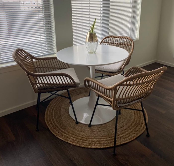 A reviewer's chairs made from light tan woven rattan, square-shaped with black metal legs, placed around a white tulip table with a woven circular mat underneath.
