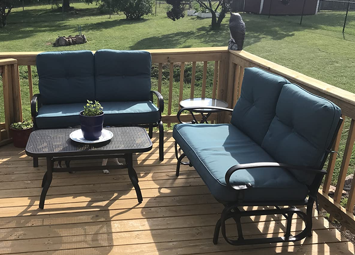 Two wrought iron love seats surrounding an oval wrought iron table on a wooden outdoor porch
