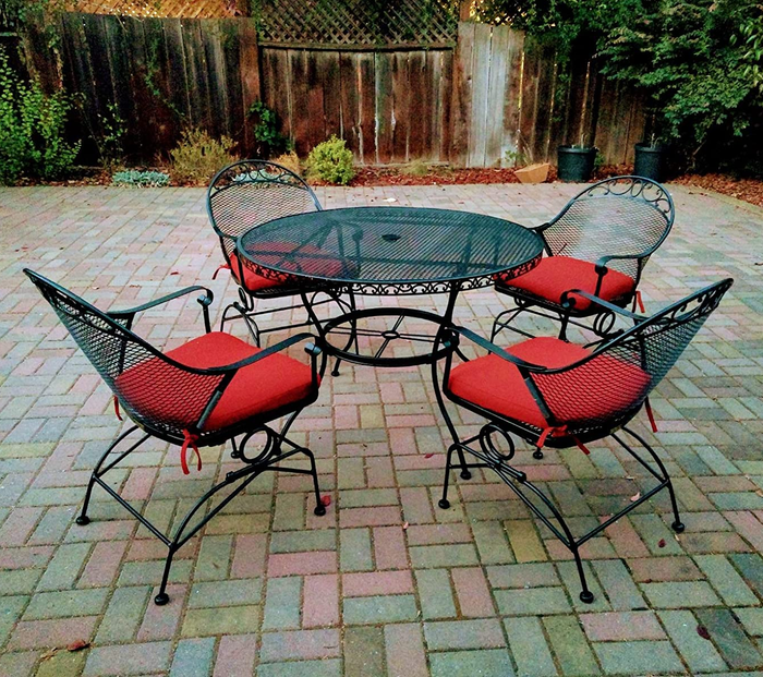 A review image of round wrought iron chairs with red cushions, arranged around a circular table outdoors