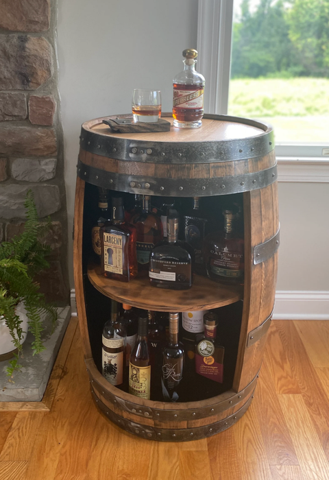 Brown barrel-style cabinet with an opening, neatly stocked with bottles inside