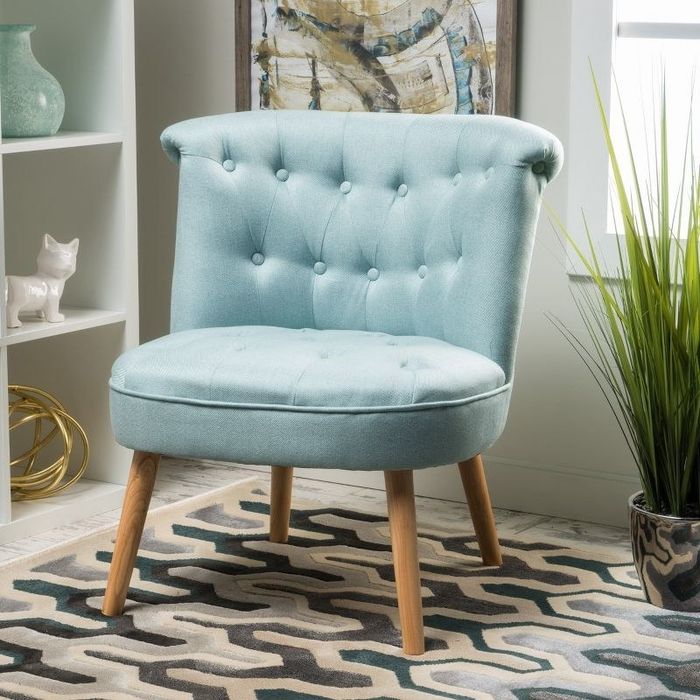 An image of a blue round tufted accent chair featuring natural stain leg finishes.