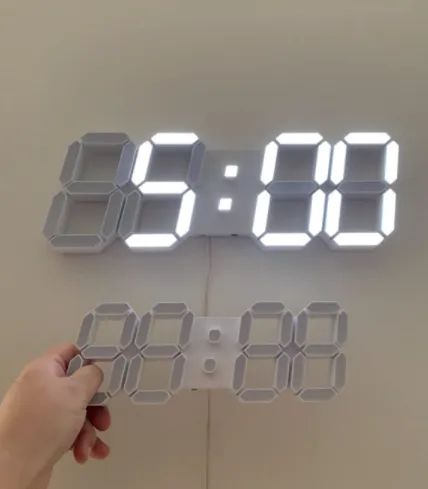 A reviewer holding the 9.5-inch version of the LED clock with the 15-inch version mounted on the wall behind it