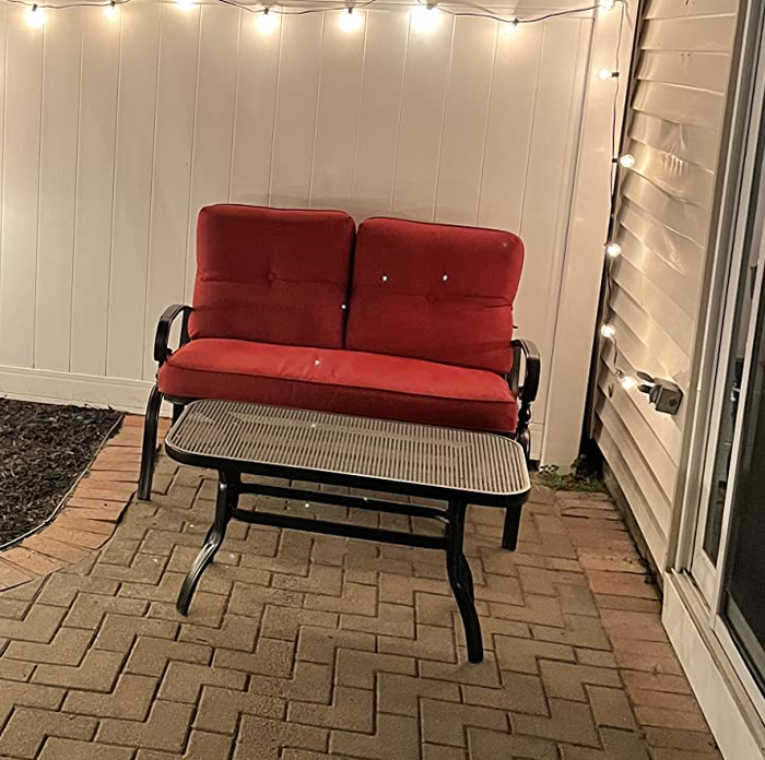 A review image of a black wrought iron loveseat with red cushions and a black metal coffee table placed outside