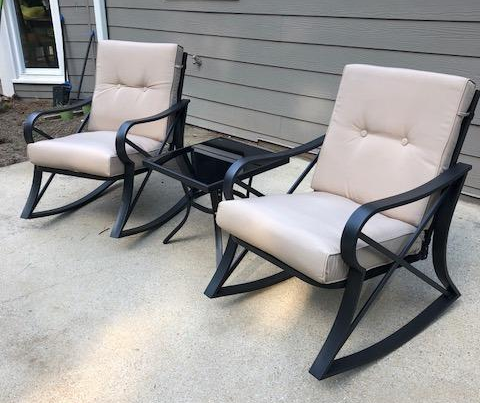 Two black wrought iron chairs with cream cushions placed between a square glass table