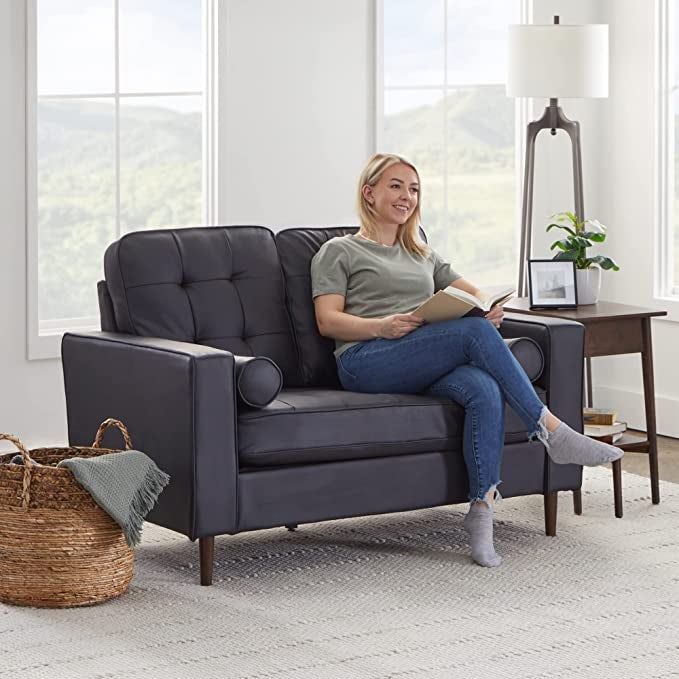 Model relaxing on a black faux leather loveseat