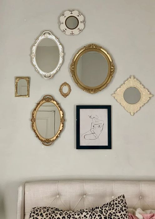 The white and gold versions of the mirror hung on a wall, paired with art and other mirrors to create a gallery wall effect