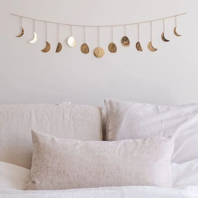 The gold hammered metal moon phase garland hanging above a bed