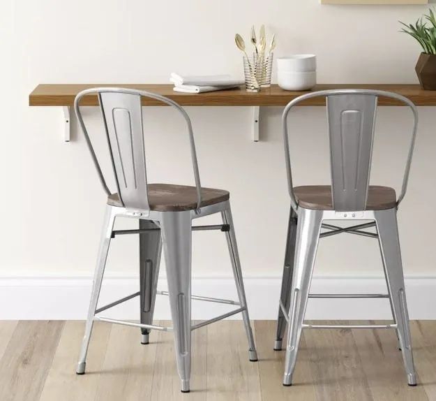 Two silver metal bar stools with backrests and wooden seats, placed in front of a bar