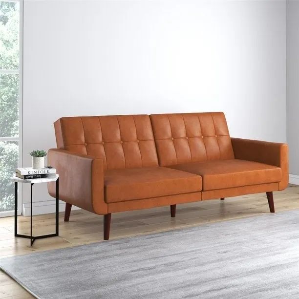 A tan faux leather futon placed in a cozy room.