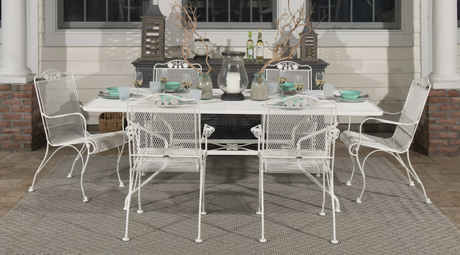 Six white wrought iron patio chairs surrounding a rectangular table outdoors