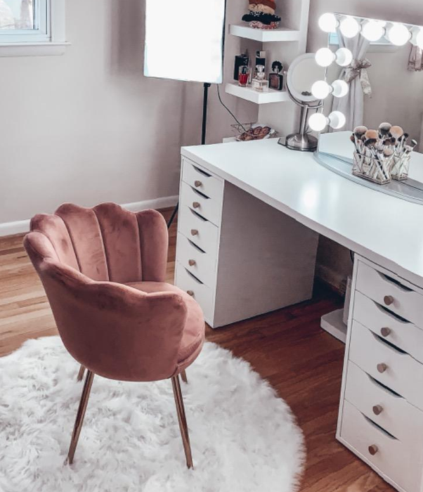 A photo of the pink chair placed in front of a vanity, showing off its soft color and inviting design.