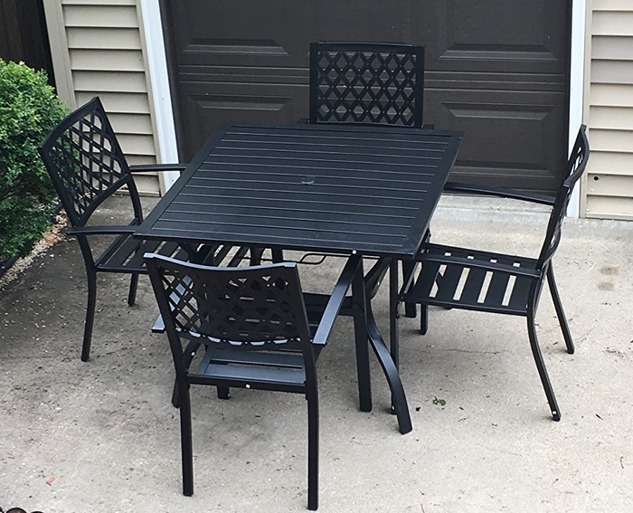 A reviewer image featuring four black wrought iron chairs arranged around a square iron table on pavement