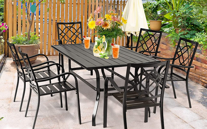 Six black wrought iron chairs surrounding a large rectangular wrought iron table outdoors in the backyard