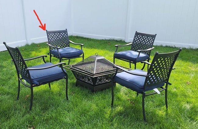 A review image of four black wrought iron chairs with blue cushions placed on grass surrounding a fire pit