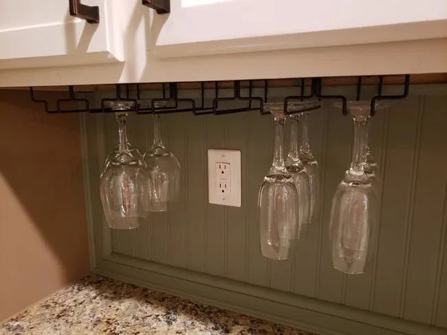 A reviewer's photo of the wineglass rack attached beneath a cabinet, with three rows of glasses hanging from it