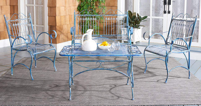 A blue antique-style wrought iron loveseat and chairs arranged around a matching rectangular table outside on a rug