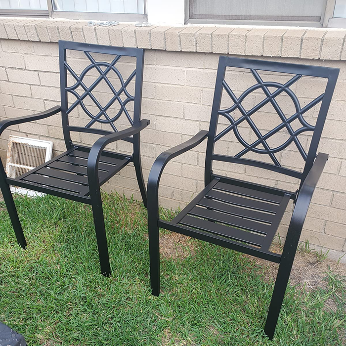 A review image of black wrought iron chairs with armrests set against a brick wall