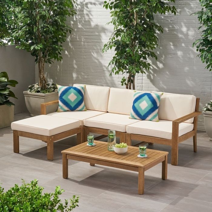 Three-seater wooden sectional with cream-colored cushions nestled in a shaded patio.
