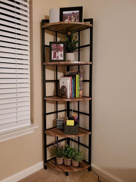 A brown wood and black five-tier shelf filled with photos, plants, and framed pictures on each level