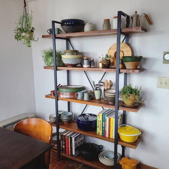 five-tier wooden shelf with a black metal frame, displaying reviewer’s cookware, books, and plants