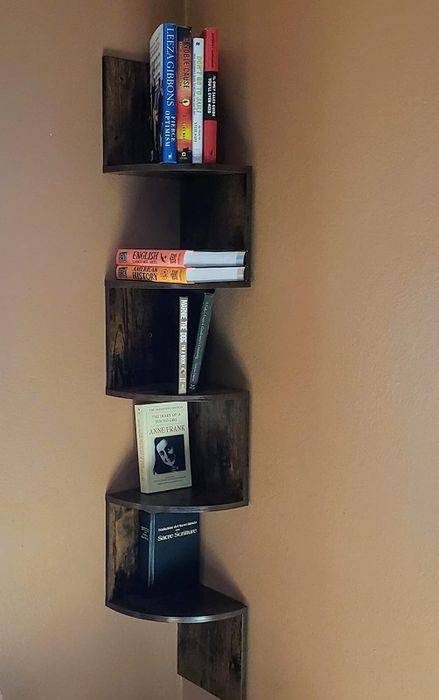 A reviewer's photo of a dark brown zigzag corner bookshelf displaying books
