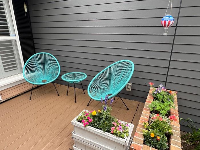 Two contemporary turquoise chairs with a matching side table on a deck, surrounded by vibrant flower pots and a hot air balloon-shaped decoration