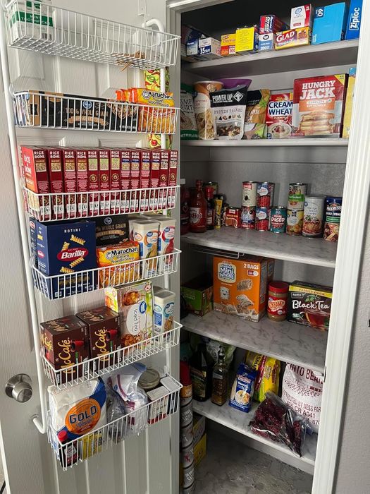 A neatly arranged pantry with shelves and door racks showcasing a variety of boxed meals, canned goods, cereals, pasta, teas, snacks, and other non-perishable food items.
