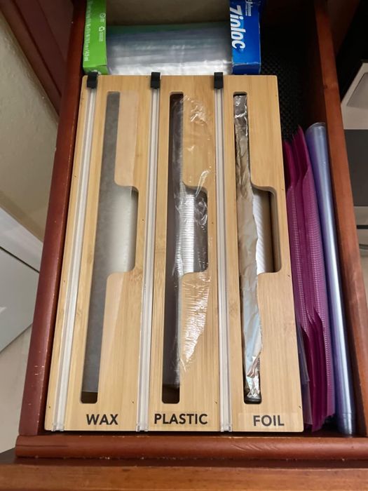 A reviewer displays the organizer in their kitchen drawer, labeled with foil, plastic, and wax paper.