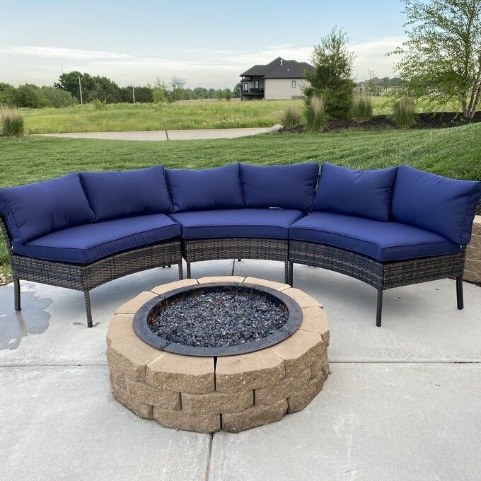 Photo of a curved sectional with navy blue cushions, set in a spacious backyard around a fire pit.