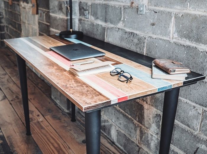 rectangular desk featuring a mix of black, light brown, white, coral, and blue wood stripes, paired with black metal legs
