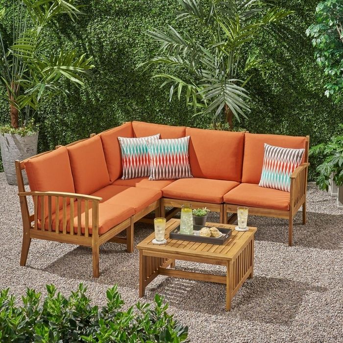 Wooden L-shaped sectional with orange cushions set in a lush, leafy outdoor patio.
