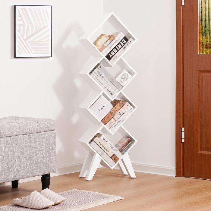 A sleek, modern white zigzag bookshelf placed against a wall, displaying books and decorative items. A gray bench and a door are also visible in the scene, featured in a shopping guide