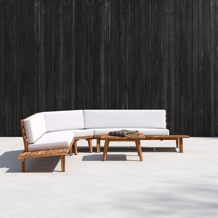 Wooden sectional with end tables and white cushions placed on a minimalist outdoor terrace.
