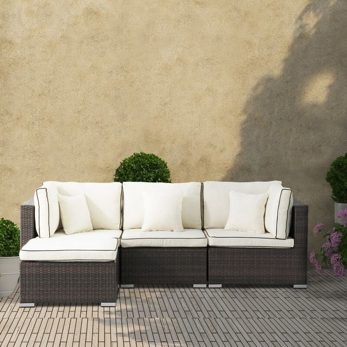 Lifestyle photo of a wicker sectional with cream cushions set on a shaded terrace.