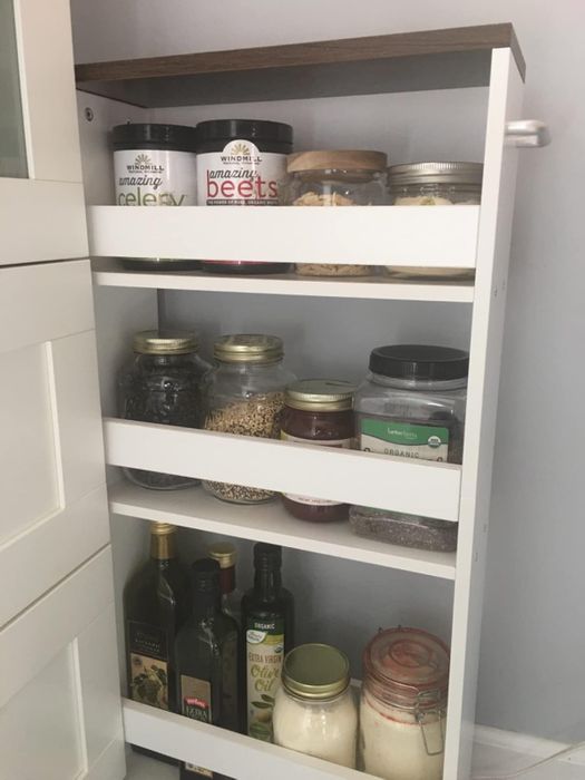 A pull-out pantry filled with various jars, including grains, spices, and oils, all neatly organized on three shelves.