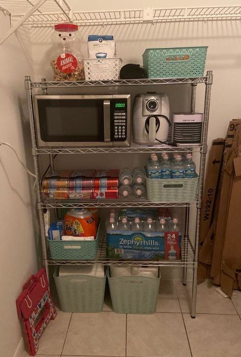 A reviewer showcases the shelving unit used in their kitchen, with a microwave and other items stored on it.