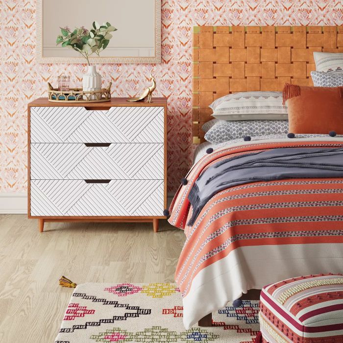The dresser with white drawers featuring a geometric texture, placed next to a bed