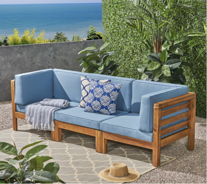 Acacia wood sofa with blue cushions set up on an outdoor terrace.