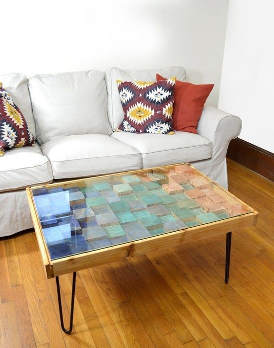 wood coffee table with metal legs and a glass top, showcasing wooden squares of various heights underneath, in a beautiful gradient of greens and blues